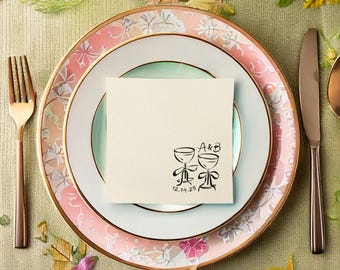 Puede incluir: Elegante mesa con un plato con estampado floral, un plato más pequeño con un centro verde menta y una servilleta crema. La servilleta presenta una ilustración negra de dos copas de champán y las iniciales "A&B" con la fecha "12.14.25".