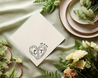 May include: A square off-white paper napkin featuring a black line drawing of two oyster shells forming a heart shape. Inside the shells are the letters C and T, with the date 09.14.24 printed in black ink above the oyster illustration.