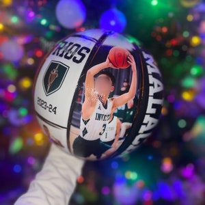 May include: White basketball with a green and gold logo that says "Warriors" and "2023-24". A photo of a basketball player in a black and white jersey with the number "3" is on the basketball.