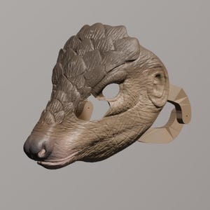 Peut inclure: Un masque d'animal brun et beige avec une surface texturée et un motif écailleux. Le masque a un large museau et une paire d'oreilles. Le masque est fait d'un matériau léger et est conçu pour être porté sur la tête.