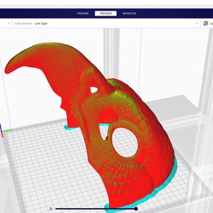 May include: A 3D model of a skull-like object is shown in a 3D printing software program. The model is red and yellow and is positioned on a blue and white grid. The software interface is visible in the background.