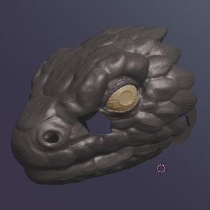 May include: A gray 3D printed model of a lizard head with a textured surface and a single yellow eye.