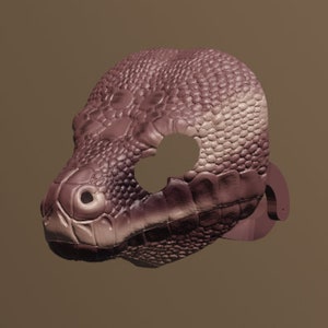 Può includere: Una maschera di serpente marrone e rosa con una superficie testurizzata. La maschera ha un foro per gli occhi e un piccolo foro per il naso.