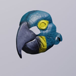 Puede incluir: Una máscara de loro azul y amarillo con un pico y agujeros para los ojos. La máscara está hecha de un material texturizado y tiene un diseño realista.