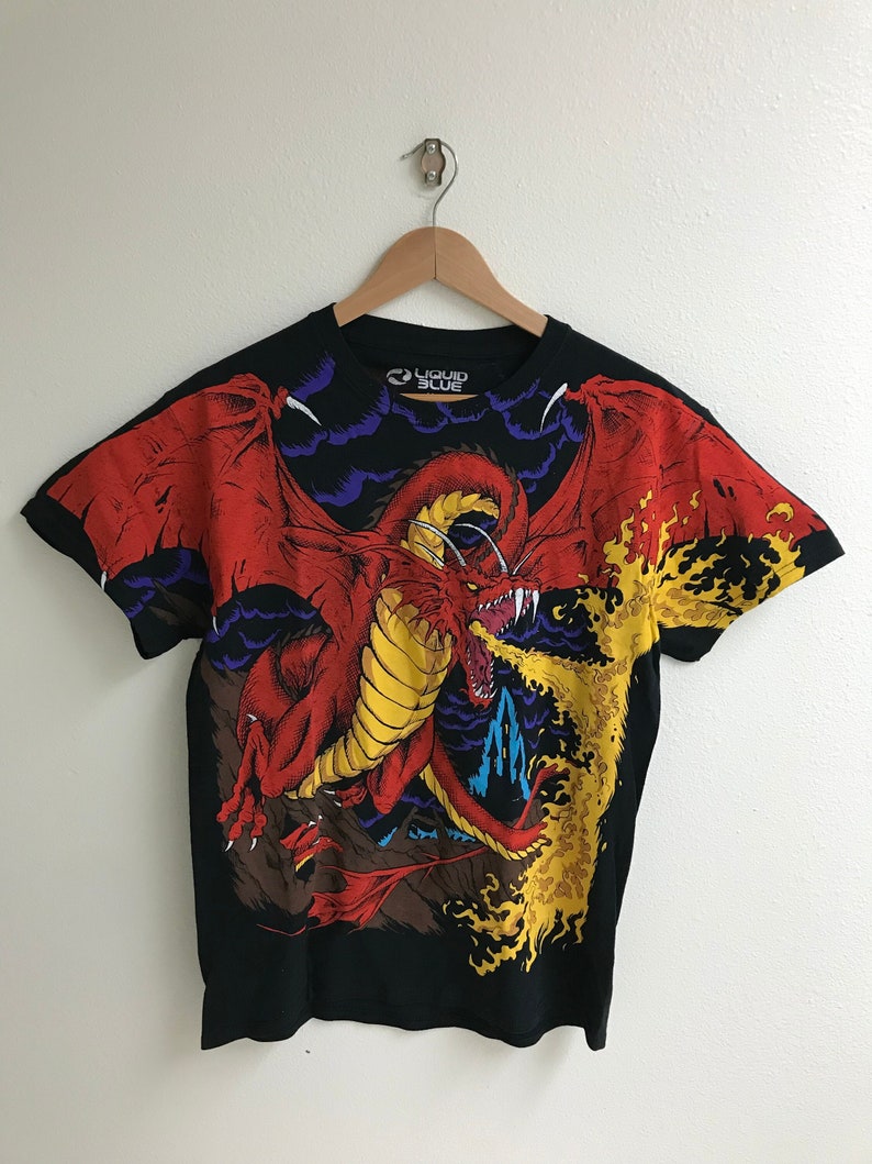 May include: Black t-shirt with a red dragon breathing fire. The dragon is surrounded by clouds and flames. The shirt has the text "Liquid Blue" on the front.