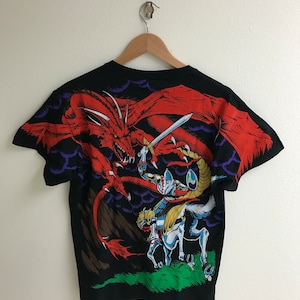 May include: Black t-shirt with a graphic print of a knight on horseback fighting a red dragon. The dragon is flying in the air and the knight is holding a sword.