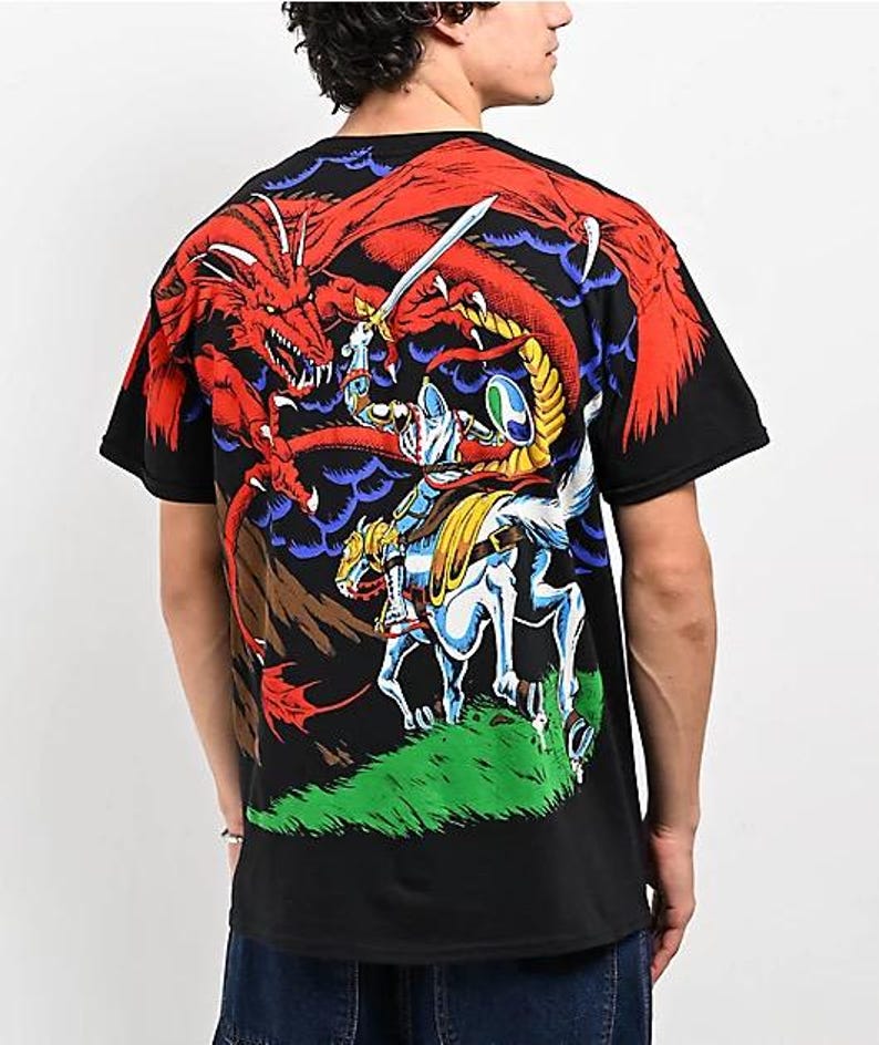 May include: Black t-shirt with a graphic print of a knight on horseback fighting a red dragon. The dragon is breathing fire and the knight is holding a sword.