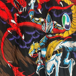 May include: A knight on horseback battles a red dragon with a sword. The knight is wearing silver armor and a blue helmet. The dragon is flying in the air with its claws outstretched. The background is a dark blue and purple sky with clouds.