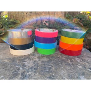 Peut inclure: Un assortiment de rouleaux de ruban adh&eacute;sif de diff&eacute;rentes couleurs, dont argent, or, noir, blanc, bleu, vert, jaune et rouge.