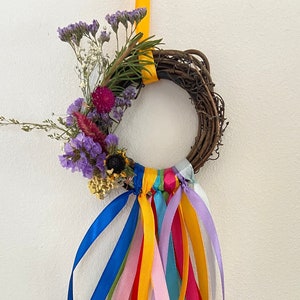 May include: A small wreath made of twigs with dried flowers and a variety of colorful ribbons hanging from it.