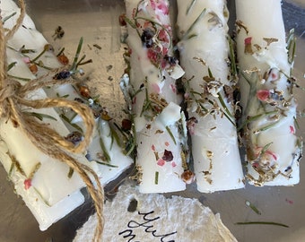 Peut inclure: Bougies blanches décorées d'herbes séchées, de fleurs et de paillettes dorées. Un ensemble est noué avec de la ficelle. Une étiquette manuscrite indique "Yule & New Year manifestation candles."