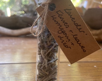 May include: A small glass jar filled with dried lavender and leaves. A brown paper tag is tied to the jar with twine and reads "Lavender: Flowers + leaves, Unmegas dried".