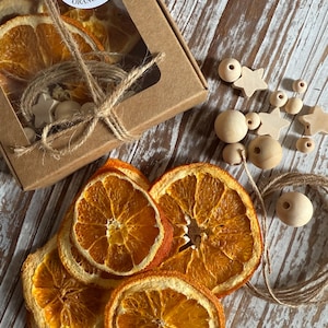May include: A craft kit for making an orange garland. The kit includes dried orange slices, wooden beads, star-shaped wooden accents, and twine. The box has a clear window and a label that reads "Craft Your Orange Garland."