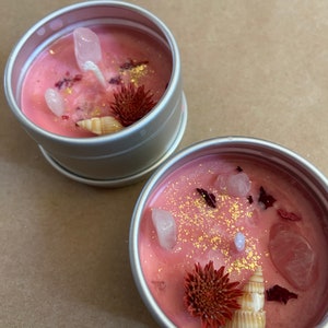May include: Two pink candles in silver tins with gold glitter, dried flowers, and small seashells.