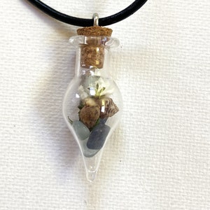 May include: A glass bottle pendant necklace with a cork stopper. The bottle contains small white flowers, seashells, and blue stones.