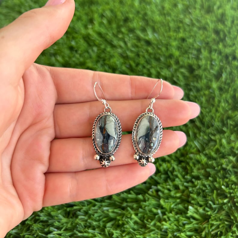 May include: A pair of silver dangle earrings with oval-shaped green and white stones. The stones have a marbled pattern and are set in a silver bezel.