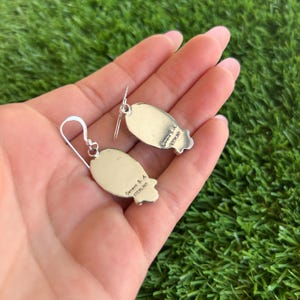 May include: A pair of silver earrings with a turquoise stone inlay. The earrings are oval shaped and have a silver hook closure. The back of the earrings are stamped with "G. Gorman & Co. Sterling".