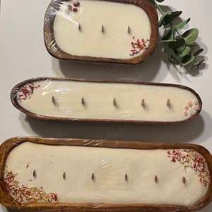 Pode incluir: Tr&ecirc;s tigelas de madeira com velas brancas e flores secas. As tigelas s&atilde;o de tamanhos e formas diferentes. As velas est&atilde;o todas acesas.