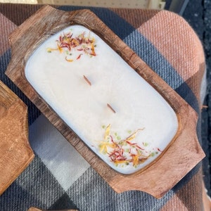 Pode incluir: Uma vela branca com flores e ervas secas em uma tigela de madeira. A tigela tem duas al&ccedil;as e &eacute; feita de madeira natural.