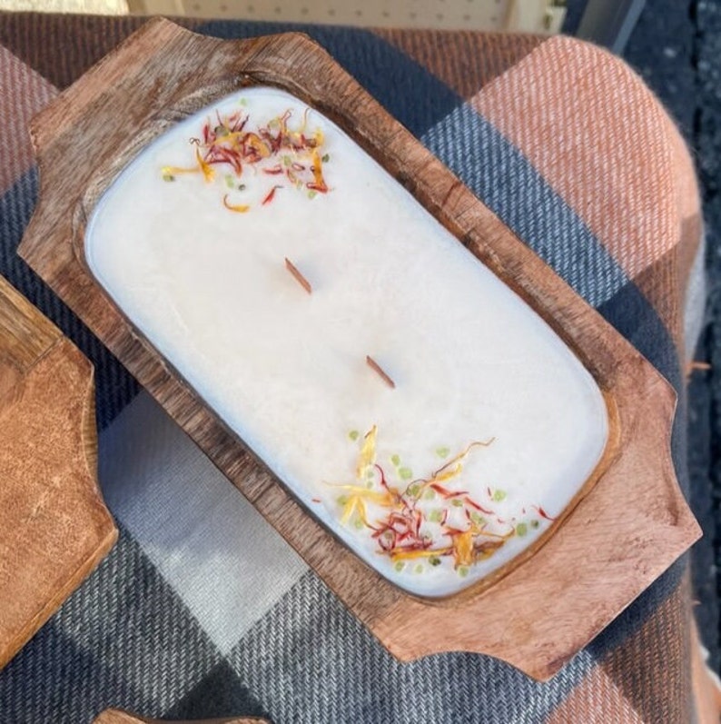 Pode incluir: Uma vela branca com flores e ervas secas em uma tigela de madeira. A tigela tem duas al&ccedil;as e &eacute; feita de madeira natural.