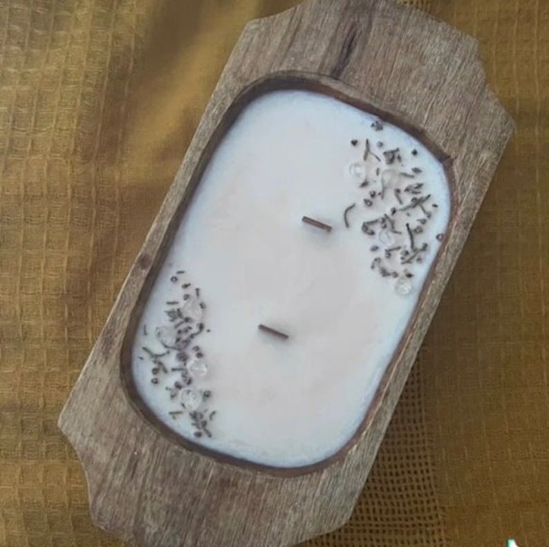 Pode incluir: Uma vela branca com flores secas e cristais incrustados na cera, sentada em uma bandeja de madeira.