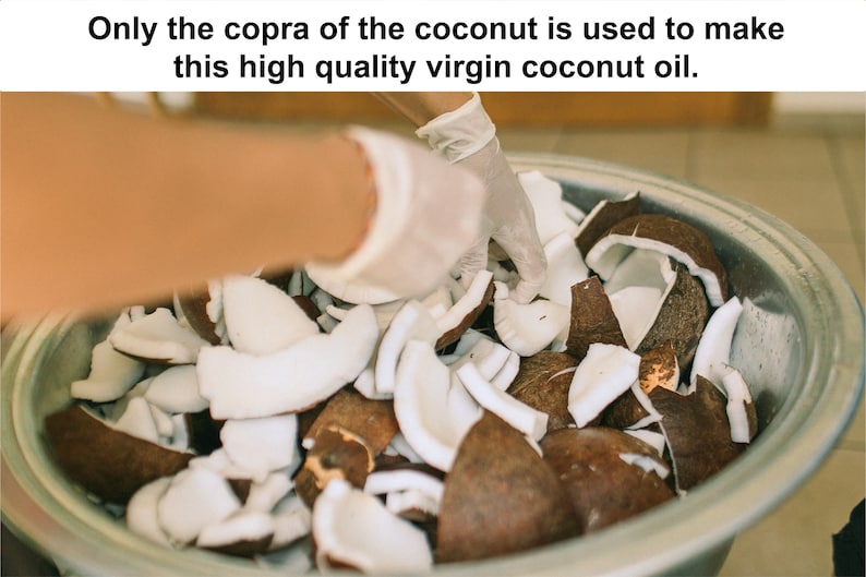 May include: A close-up of a metal bowl filled with coconut pieces. The coconut pieces are brown and white. A gloved hand is reaching into the bowl. Text at the top reads: "Only the copra of the coconut is used to make this high quality virgin coconut oil."