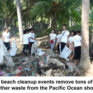 May include: A group of people wearing white t-shirts with text are cleaning up trash on a beach. They are holding large bags and removing waste from a pile of debris. The scene is set on a sunny day with palm trees in the background.