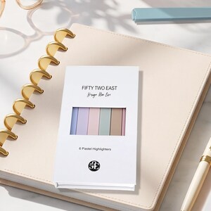 May include: A white rectangular box containing six pastel highlighters in blue, purple, pink, green, and brown. The box features the text FIFTY TWO EAST, Design Plan Life, 6 Pastel Highlighters, and a circular logo with the letters 52E.