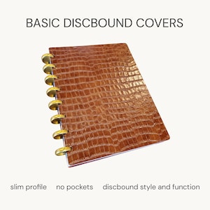 May include: A brown discbound notebook cover with a textured crocodile skin pattern and gold-colored binding discs. The text reads BASIC DISBOUND COVERS, slim profile, no pockets, discbound style and function. The cover has a rectangular shape.