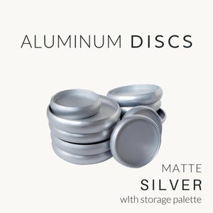 May include: A stack of circular aluminum discs with a matte silver finish. The text on the image reads ALUMINUM DISCS, MATTE SILVER, and with storage palette. The discs are arranged in a pile with one disc positioned upright to the side.