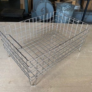 May include: A silver wire mesh basket with a rectangular shape and four legs. The basket is made of a sturdy wire mesh and has a smooth, polished finish.