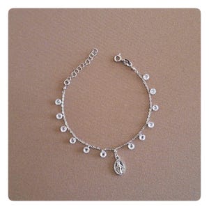 May include: A silver chain bracelet with a small silver charm of the Virgin Mary and clear crystal beads.