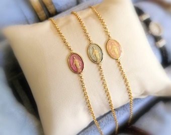 Puede incluir: Tres pulseras de cadena dorada con dijes ovalados que representan una imagen religiosa. Los dijes son de color rosa, azul y dorado.