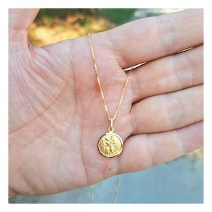 May include: A gold chain necklace with a round pendant featuring a detailed image of a saint. The pendant is attached to a delicate chain.