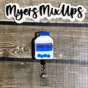 May include: A white and blue badge reel with a bottle design that says "HAPPY PILLS". The badge reel has a clear plastic strap and a black retractable cord. The text "Myers Mix Ups" is above the badge reel.