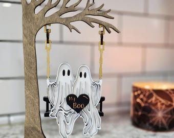 May include: A wooden Halloween decoration featuring two white ghosts on a swing, with the words "My Boo" on a black heart. The swing hangs from a wooden tree, all set on a black base.