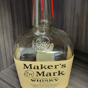 May include: A clear glass Maker's Mark Kentucky Straight Bourbon Whisky bottle with a distinctive red wax seal dripping down the neck. The cream-colored label features black text and a 1.75 liters volume marking, with a wax-sealed cap on top.