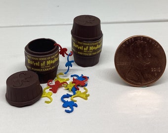 Puede incluir: Un juego de barril de madera marrón llamado "Barrel of Monkeys" con piezas de mono amarillas, azules y rojas esparcidas alrededor del barril. El juego está diseñado para poner a prueba tu firmeza y equilibrio.