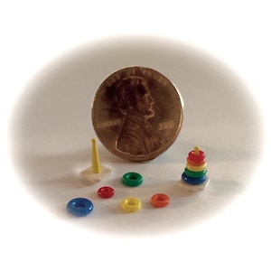 May include: Miniature toy set with a penny for scale. Includes a stacking ring toy with red, yellow, green, and blue rings, a peg toy, and several colourful rings. The toys are small and brightly coloured.