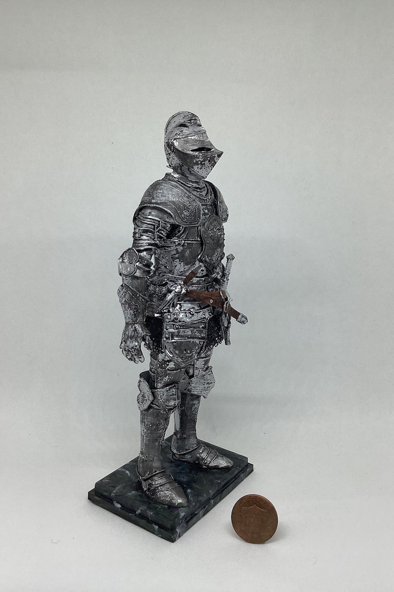 May include: A silver knight figurine standing on a green marble base. The knight is wearing full armor and holding a sword. A penny is in the foreground for scale.