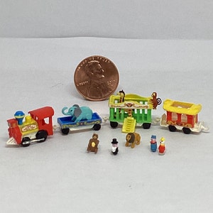 May include: A miniature toy train set with a red and yellow engine, a blue and white elephant car, a green and yellow cage car with a giraffe and monkey, a red and yellow car, and several miniature figures including a bear, a clown, and a lion.