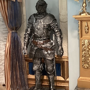 May include: A silver knight statue with a detailed design, standing on a black marble base. The statue is in a room with a gold and white decorative fireplace and a blue and white patterned curtain.