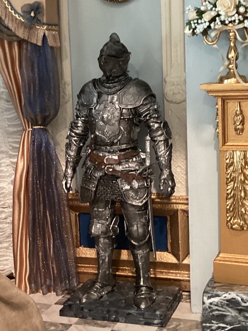 May include: A silver knight statue with a detailed design, standing on a black marble base. The statue is in a room with a gold and white decorative fireplace and a blue and white patterned curtain.