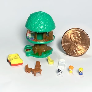 May include: A miniature plastic treehouse playset with a green canopy and brown trunk, accompanied by a yellow car, brown furniture, a white lounge chair, two small figures, a dalmatian dog, and a 2022 US penny for scale reference.