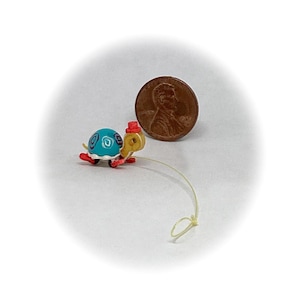 May include: A small, blue and white toy turtle with a red hat and wheels. The turtle is pulled by a string.