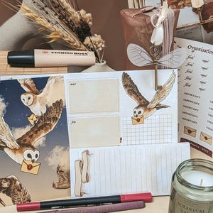 Peut inclure: Divers articles de papeterie, dont un surligneur, des stylos et des blocs-notes. Les blocs-notes présentent des illustrations de hiboux portant des lettres. Une clé décorative et une bougie avec le texte "Botanical Garden" sont également présentes.