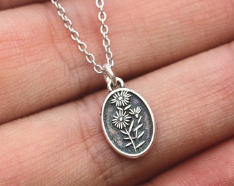 May include: A silver chain necklace with a small oval pendant featuring a delicate floral design.