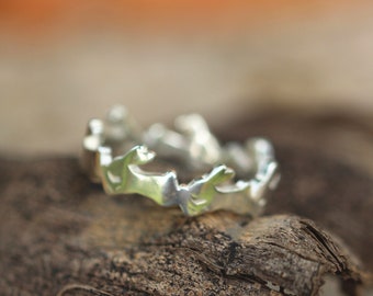 May include: A silver ring with a unique, jagged design. The ring is made of metal and has a shiny finish.
