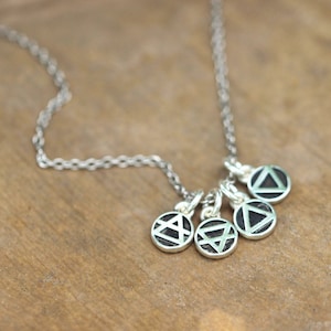 Może przedstawiać: Srebrny łańcuszek z pięcioma srebrnymi zawieszkami. Każda zawieszka to koło z innym geometrycznym wzorem w środku. Wzory są czarno-białe.