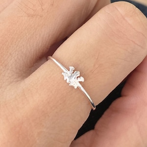 Puede incluir: Un anillo de plata con un diseño delicado y abstracto. El anillo se lleva en un dedo.